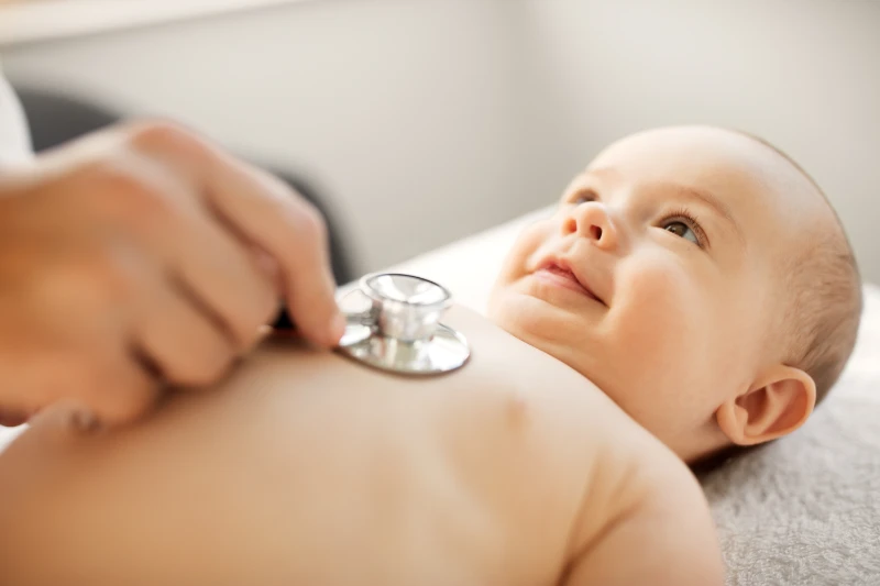 baby laying down smiling with a stethoscope on his chest