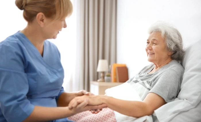 Older woman resting in bed younger woman holding her hand