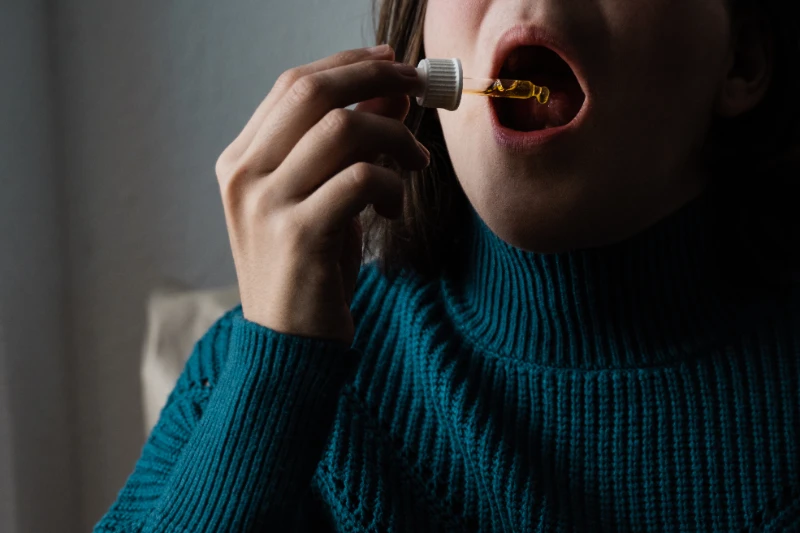 a woman wearing a blue sweater dropping oil under her tongue