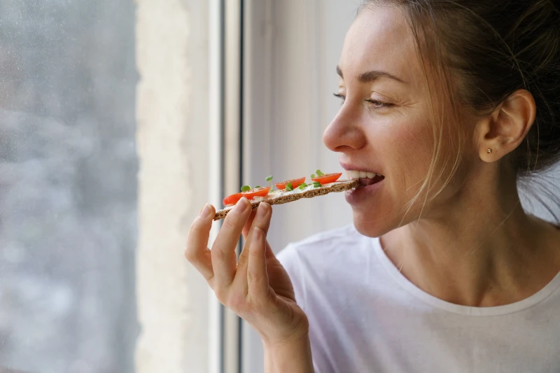 a woman sitting by the window eating a plant based item